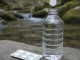 Weiße Entkeimungstablette schwebt über dem geöffneten Hals einer klaren Wasserflasche auf einem Felsen am Bach, daneben ein unbedruckter Blisterstreifen mit weiteren Tabletten.