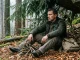 Person sitzt auf einer dicken Laubunterlage in einem windgeschützten Waldplatz.