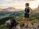 Trailrunnerin mit Laufweste und Trinkgürtel auf einem alpinen Aussichtspunkt, daneben ein Laufrucksack.
