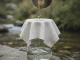 Trübes bräunliches Wasser wird aus einem Metallbecher durch ein über ein Glas gespanntes Baumwolltuch gegossen; unter dem Tuch läuft es klar in das Glas.