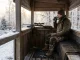 Jäger beim Ansitz im Winter auf einer isolierten Hochsitzkanzel mit Decke, warmen Stiefeln und Thermobecher.