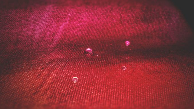 Makroaufnahme eines roten Funktionsgewebes, auf dem einzelne Wassertropfen als Kugeln stehen, ohne einzuziehen