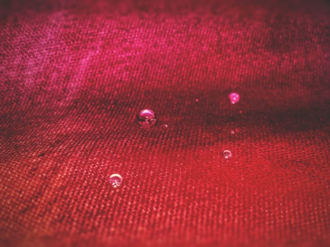 Makroaufnahme eines roten Funktionsgewebes, auf dem einzelne Wassertropfen als Kugeln stehen, ohne einzuziehen